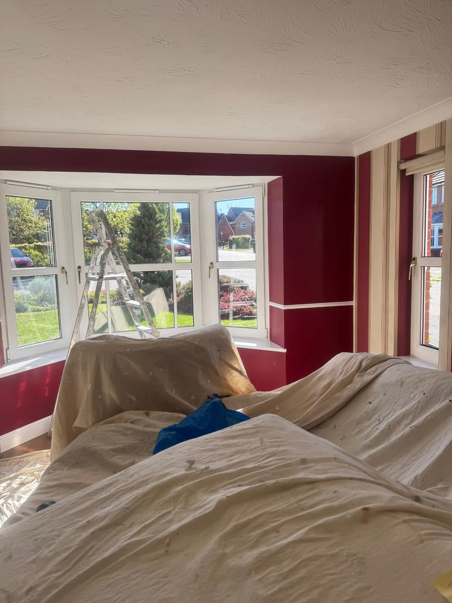 Bay window lounge in Bonnyrigg repainted in burgundy by W J Crighton, furniture sheeted